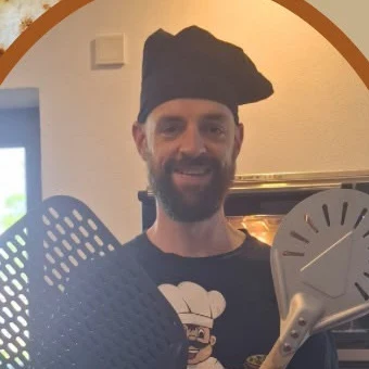 Daniel Schneider mit Kochmütze und zwei Pizzaschaufeln