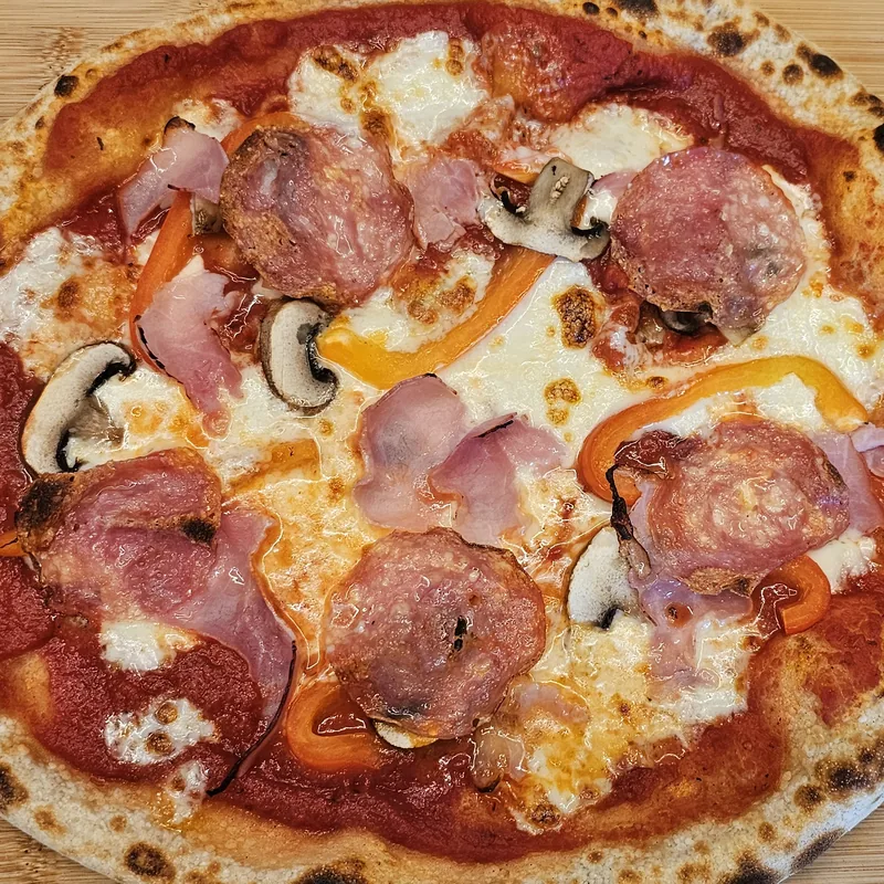 Frisch gebackene Pizza mit Schinken, Salami und Champignons auf einem Holzbrett